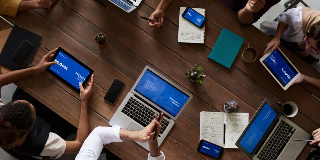 Diverse team collaborating around a meeting table with laptops and tablets.